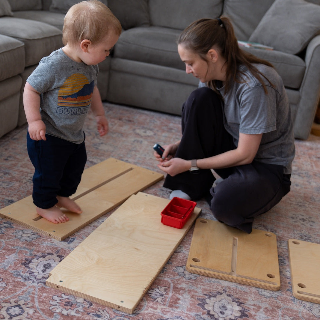 Woman and child building wooden kids furniture on a living room floor.