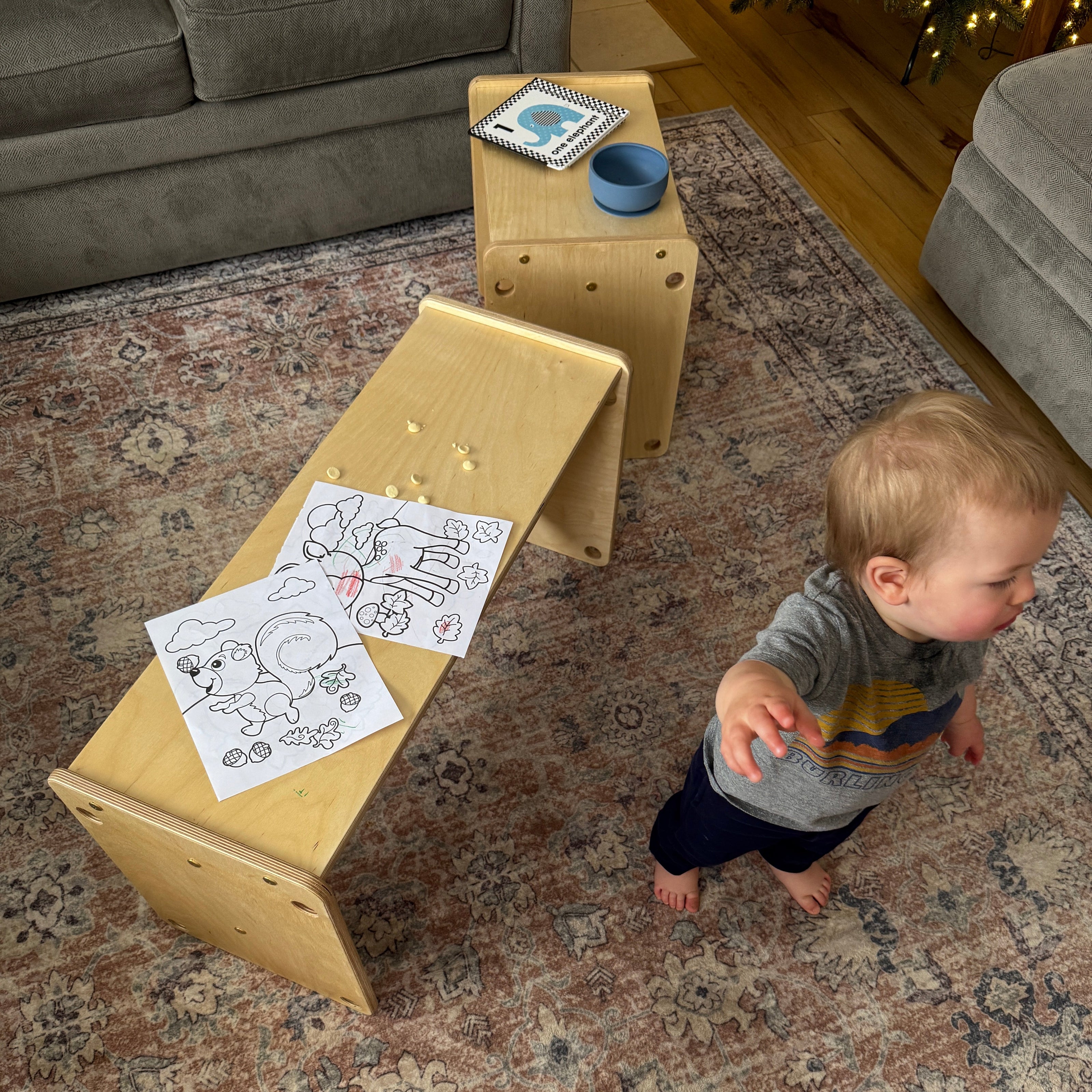 Child playing with a wooden table and chairs on a patterned rug