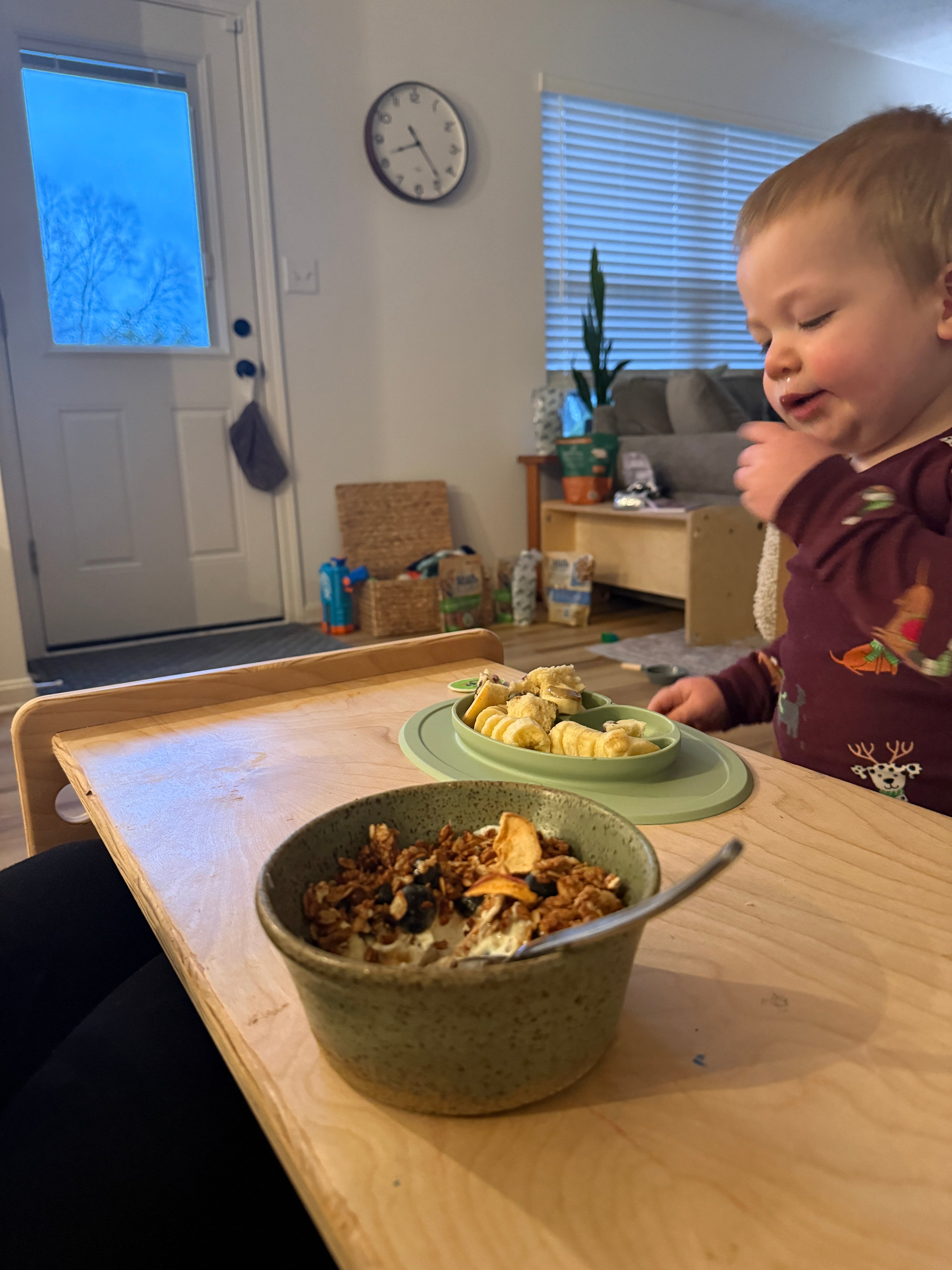Toddler eating snack independently at wooden kids table in living room