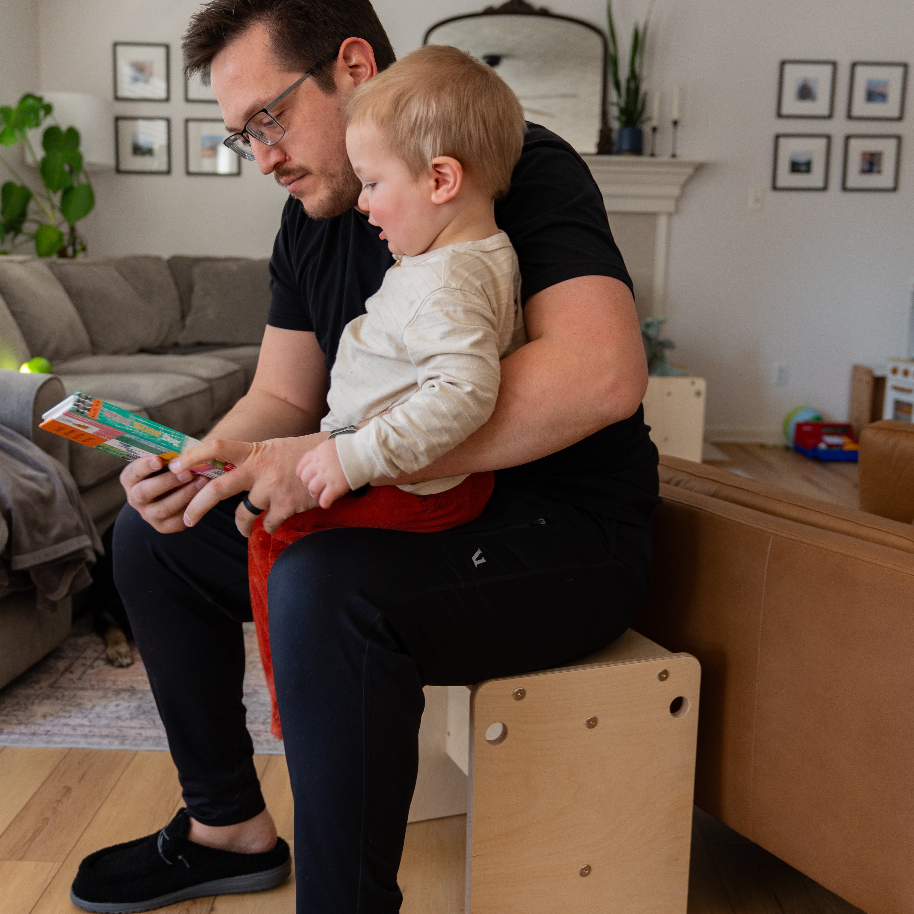 Dad sitting on wooden kids stool with toddler in living room