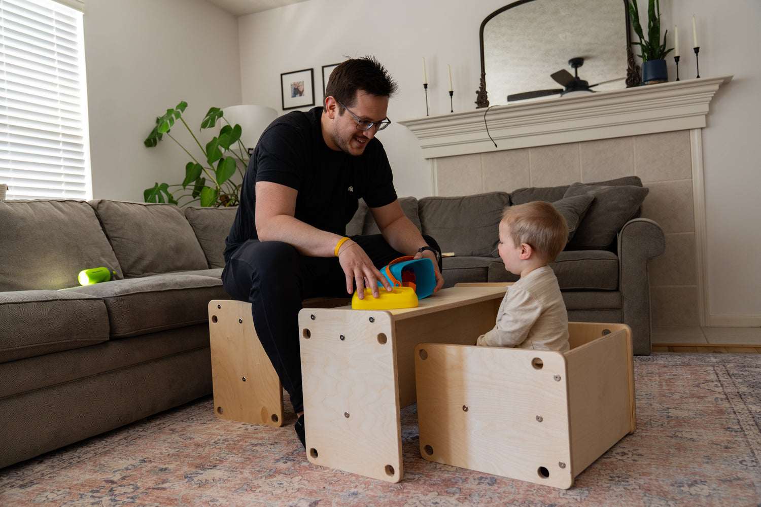 Dad playing with toddler sitting at wooden kids table in modern living room